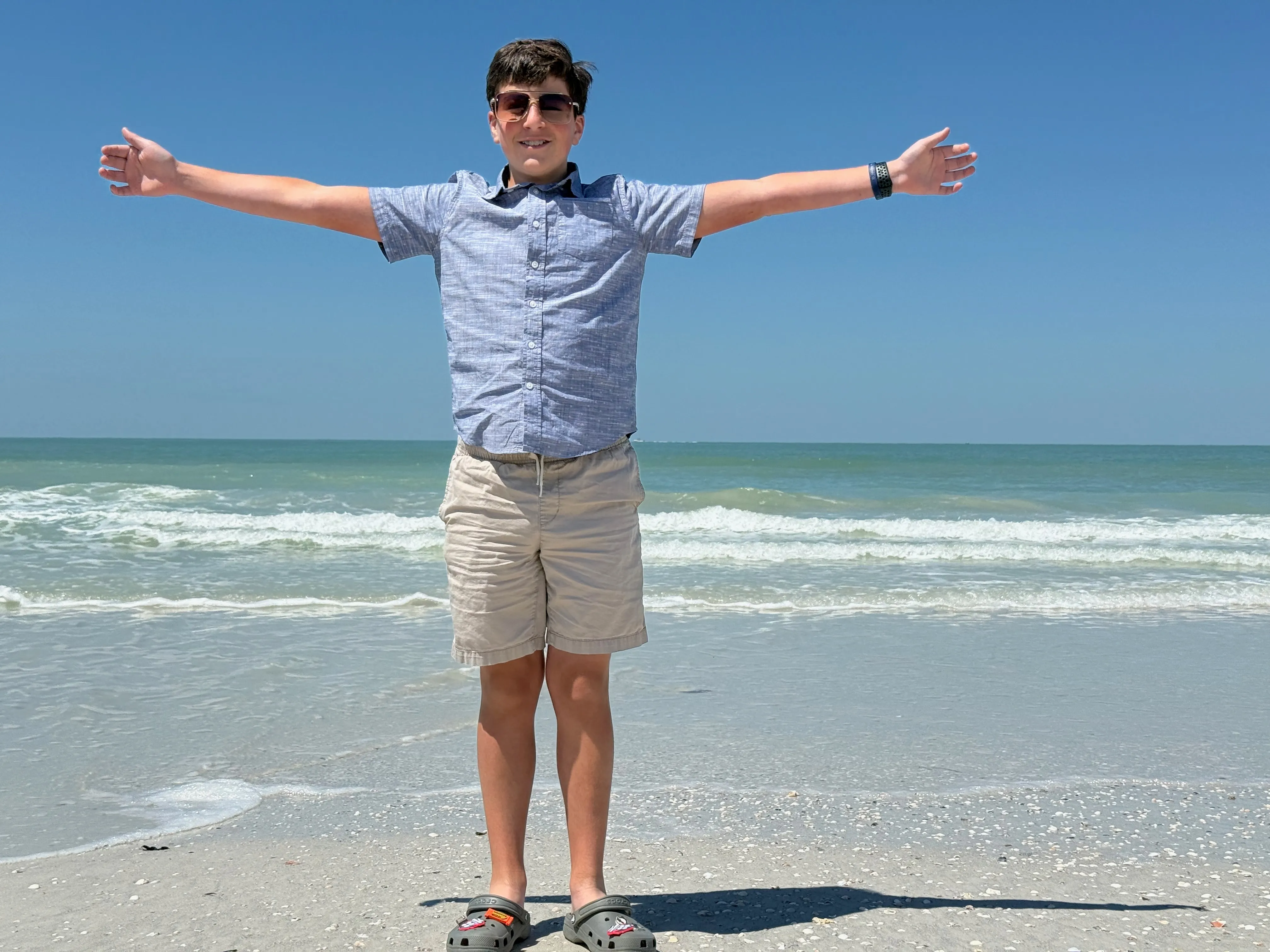 A smiling child stretches their arms wide on a sunny Tampa Bay beach by the Gulf of Mexico