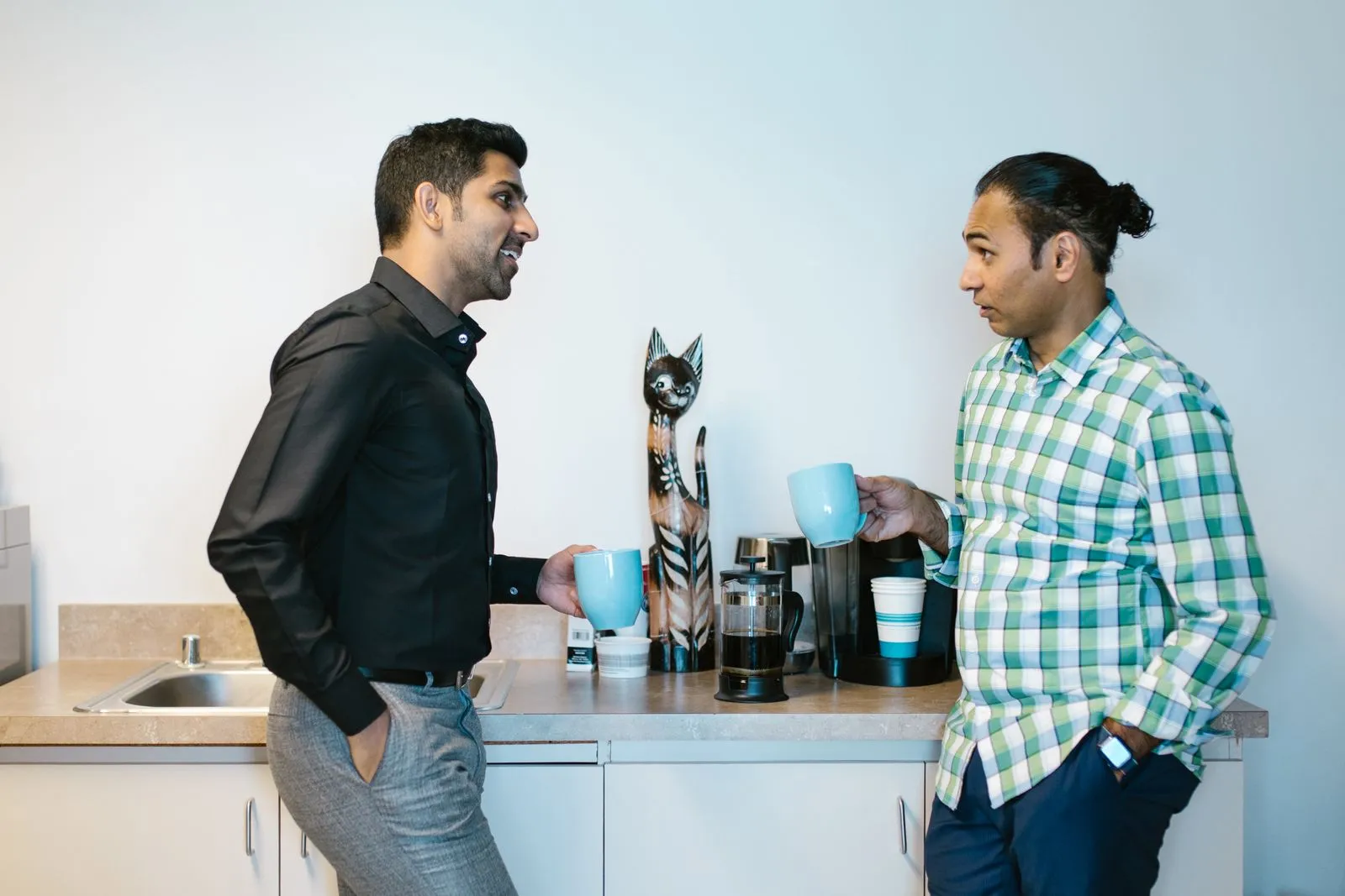 Two coworkers chatting over coffee in an office break room