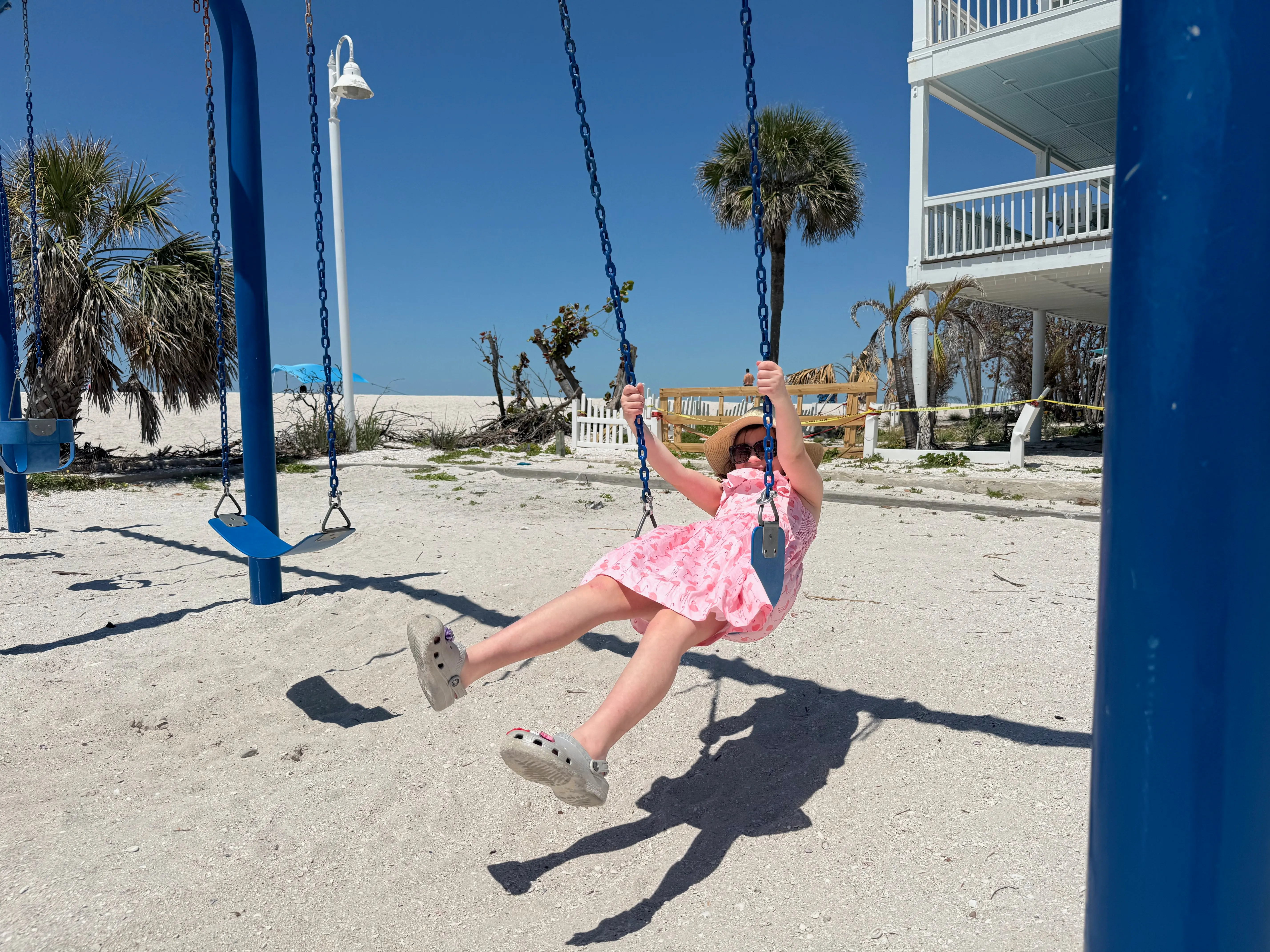 A child joyfully swinging at a sunny Tampa Bay beach, palm trees in the background