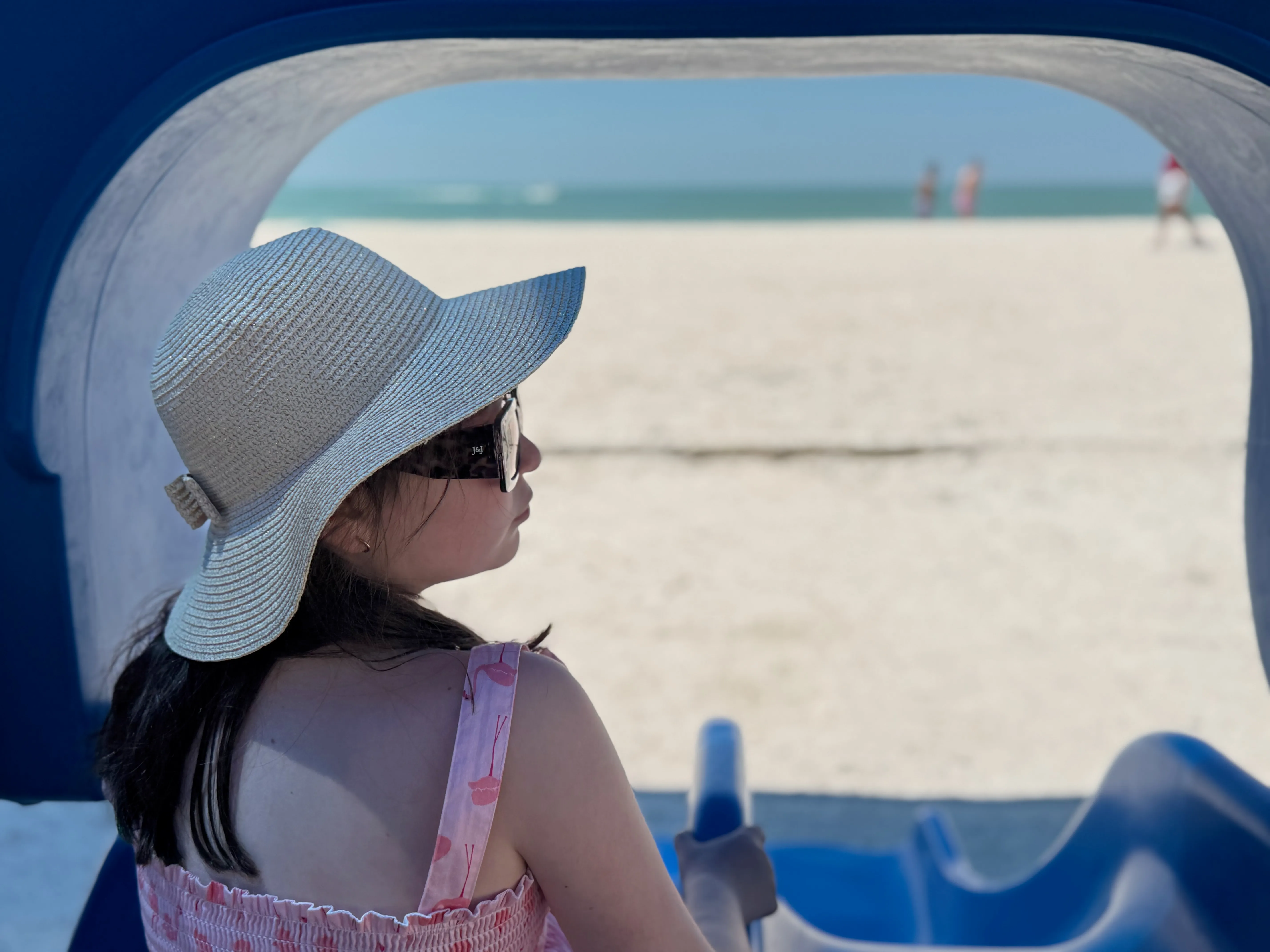 A child in a sun hat gazing out at the bright turquoise Gulf waters of a Tampa Bay beach