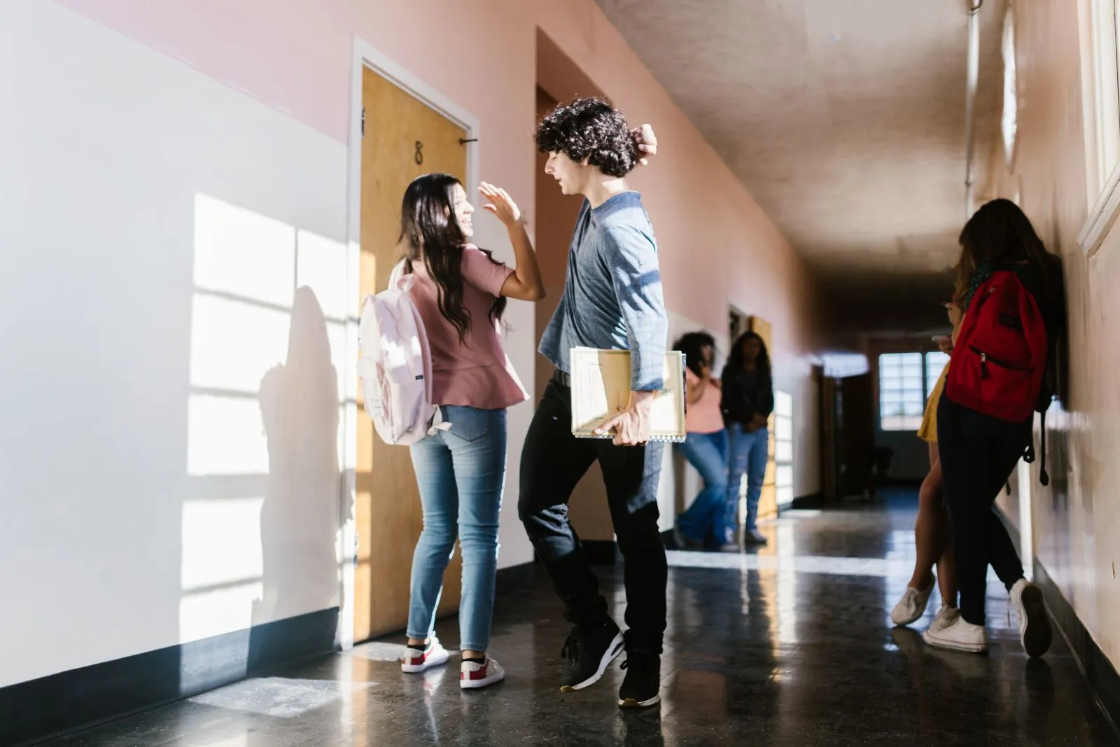 High school students greeting each other in a sunlit school hallway between classes